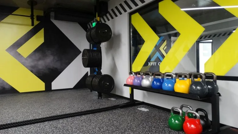 Стелаж с олимпийски дискове и цветни кетълбели върху EPDM настилка в X-Fit Club Пловдив
