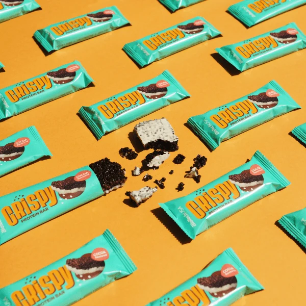 Група от BioTech USA Crispy Protein Bar с какао, подредени на фона на спортна екипировка или тренировъчна среда