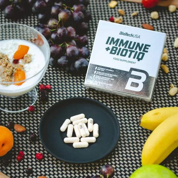 Опаковката на BioTech USA Immune+Biotiq, поставена до чаша вода, символизираща приема