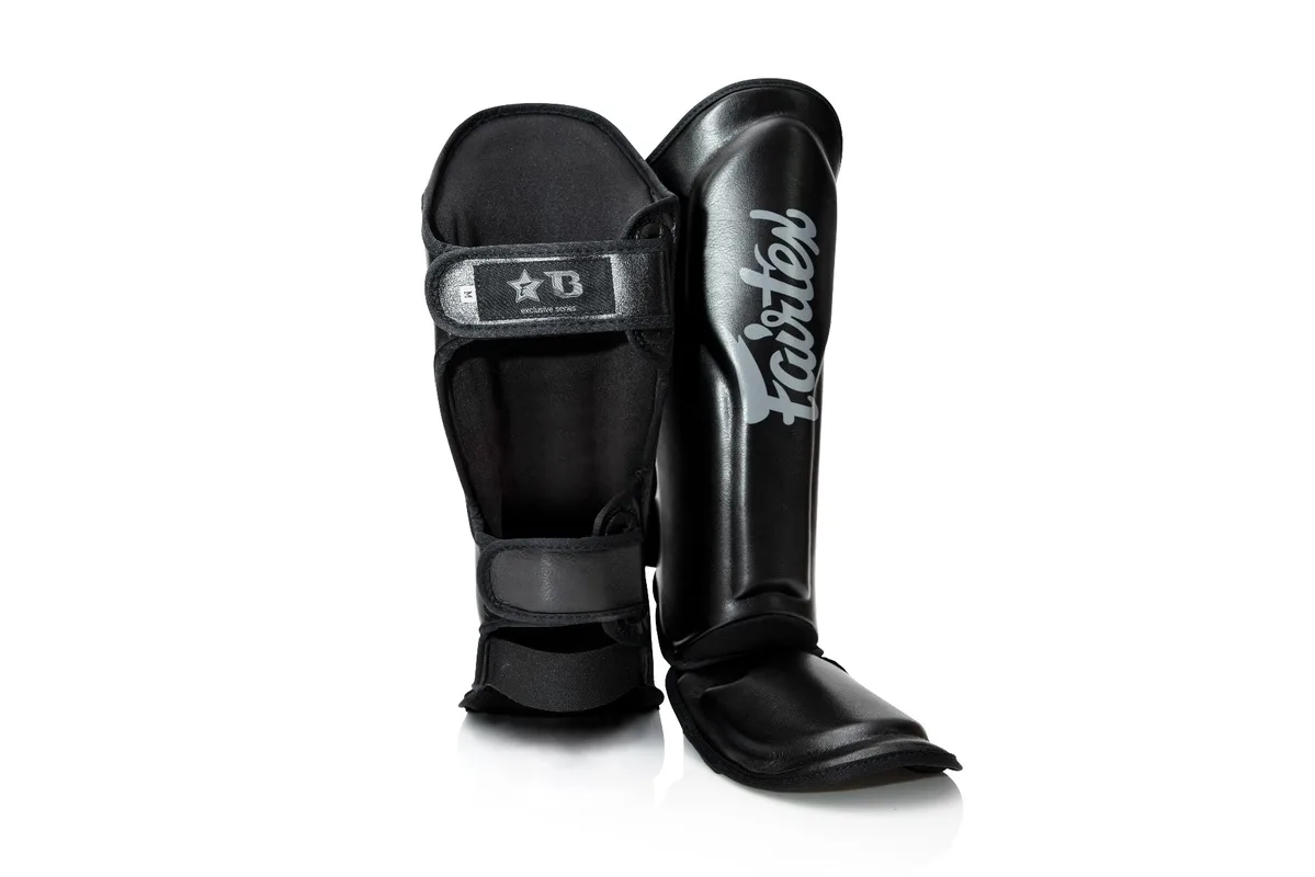 Детайлен план на логото на Fairtex x Booster върху черните протектори FXB SG, подчертаващ сътрудничеството между марките.