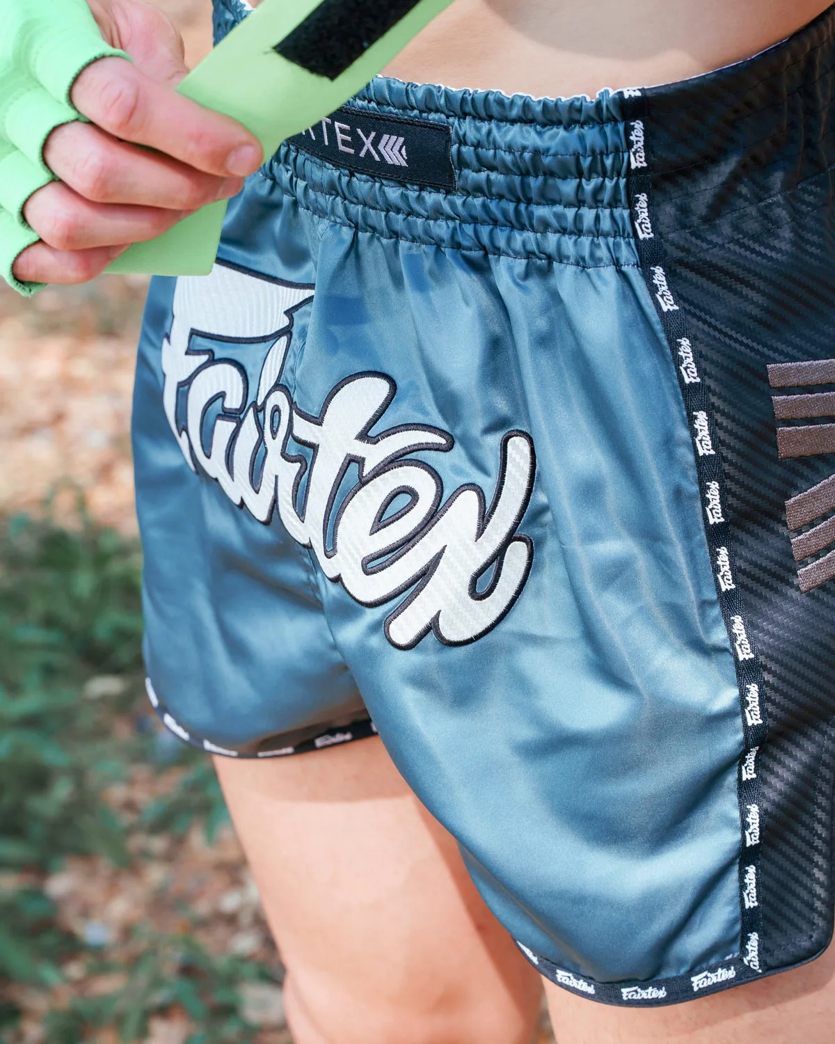 Детайлна снимка на шортите Fairtex Arokaya Special Teal Phantom, показваща ластичния колан с логото на Fairtex и текстурата на сатенената материя.
