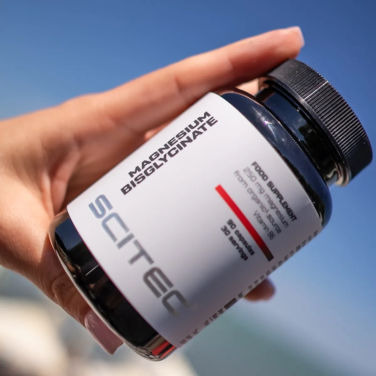 Близка снимка на капсули Scitec Nutrition Magnesium Bisglycinate, разположени до опаковката, подчертаваща формата на добавката.